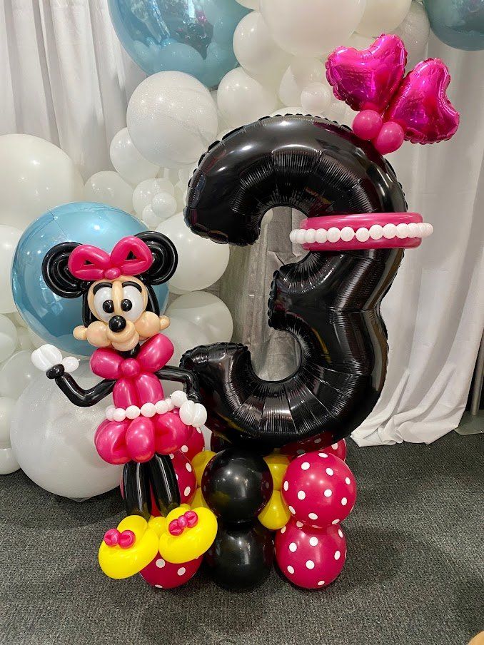 A balloon sculpture of minnie mouse standing next to a number three balloon.
