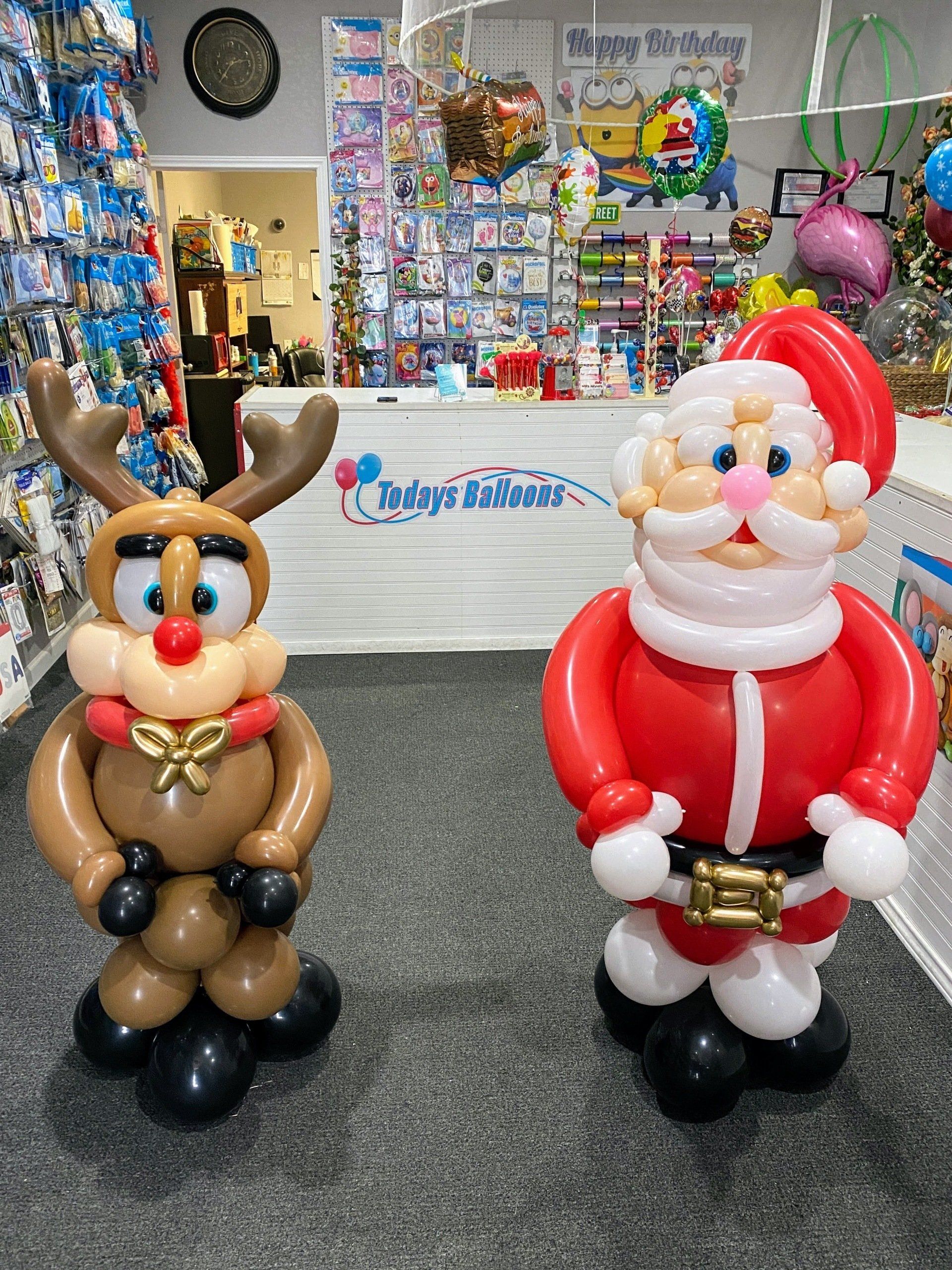 A reindeer and santa claus made out of balloons are standing next to each other in a store.