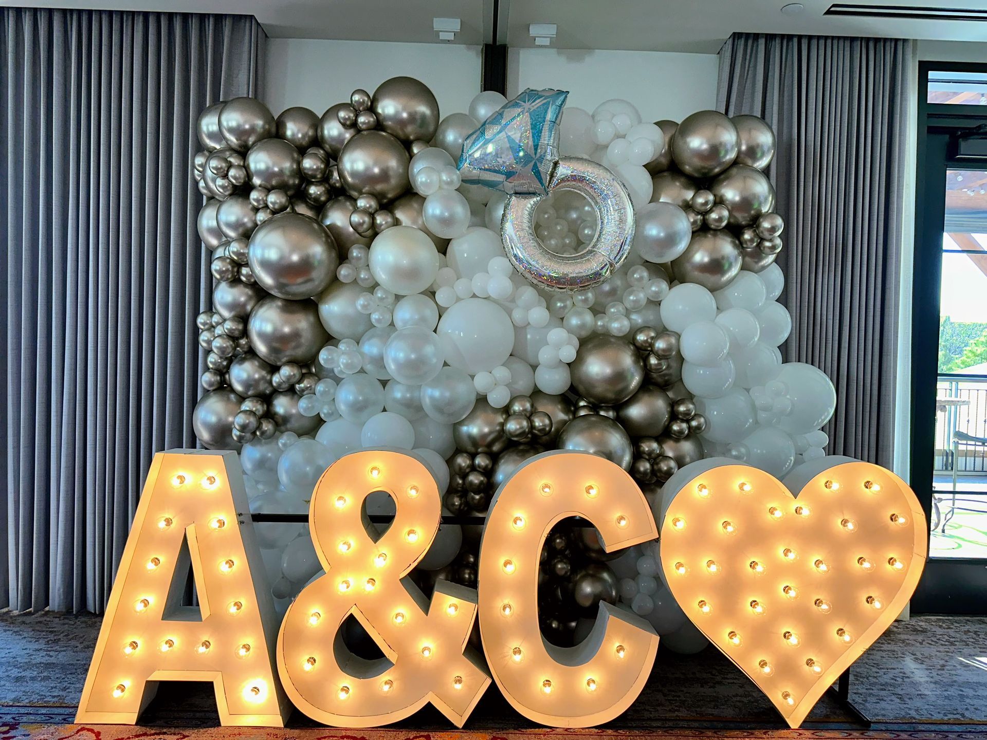 Luxury silver and white balloon wall backdrop with chrome metallic balloons, pearl white clusters, iridescent 60 foil balloon, diamond accent, paired with large illuminated marquee letters 'A&C' and heart for elegant 60th anniversary, milestone birthday, or wedding vow renewal celebration photo setup