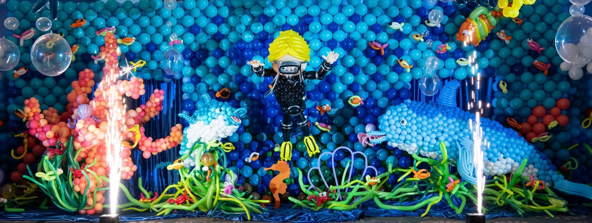 A scuba diver is swimming in the ocean surrounded by balloons.