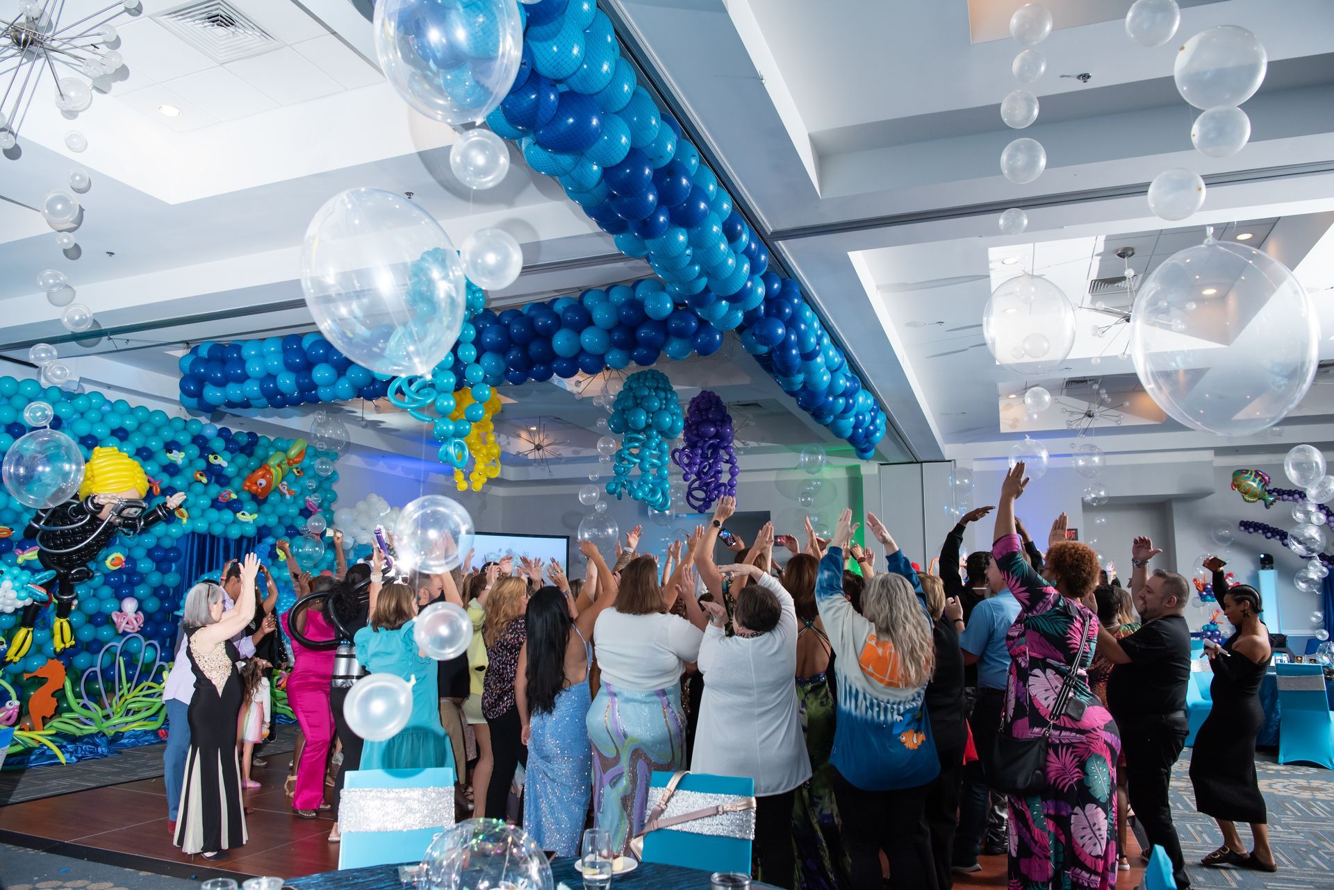 A group of people are standing in a room with balloons hanging from the ceiling.