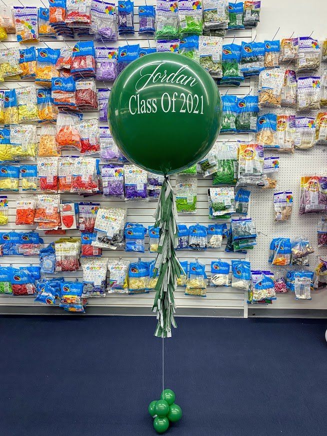 A green balloon with the words `` class of 2021 '' on it is sitting in front of a wall of balloons.