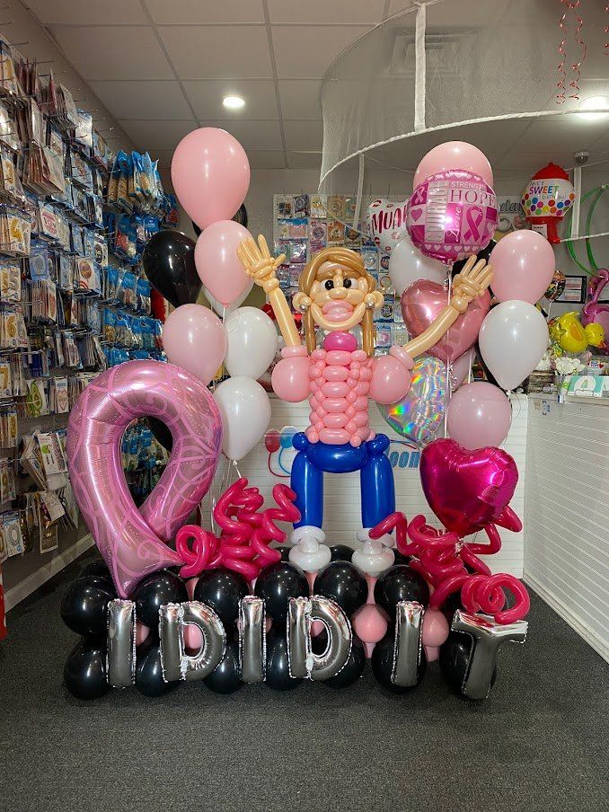 A girl made out of balloons is surrounded by pink and black balloons.
