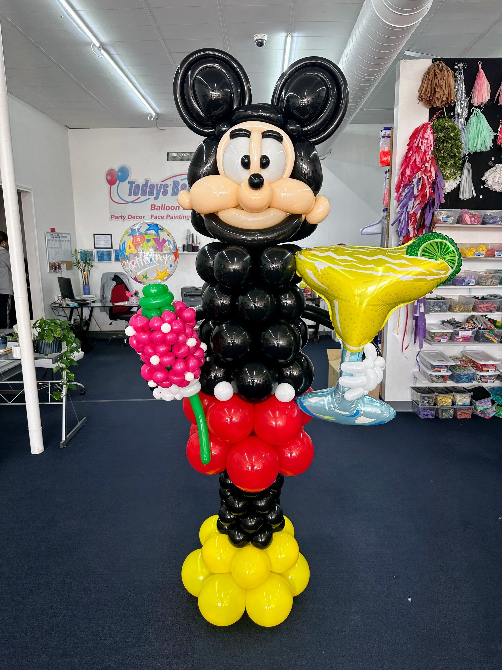 A mickey mouse made out of balloons is holding a martini glass.