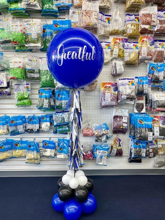 A blue balloon with the word greatful on it is sitting on top of a bunch of blue and black balloons.