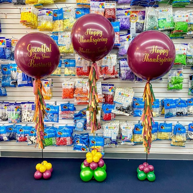 Three balloons are sitting on top of each other in front of a wall of balloons.