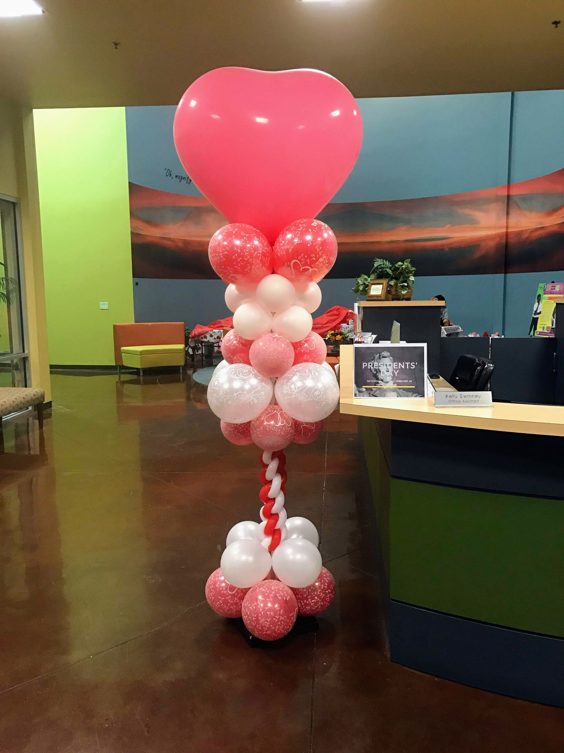 A pink heart shaped balloon is surrounded by pink and white balloons