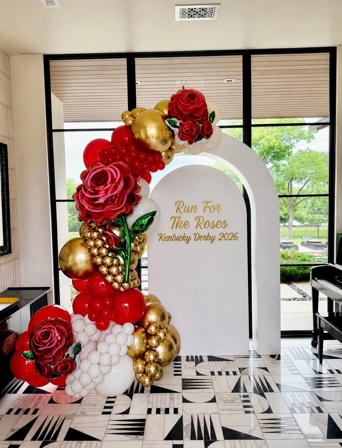 An ELEGANT RED, GOLD, AND WHITE BALLOON GARLAND WITH A ARCH BACKDROP FOR THE KENTUCKY DERBY ACCENTED WITH ROSE FOIL BALLOONS.