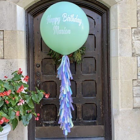 A green balloon that says happy birthday marion hangs on a door