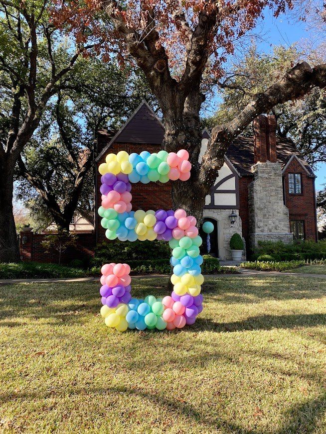 A large number 5 made of balloons is sitting in the grass in front of a house.