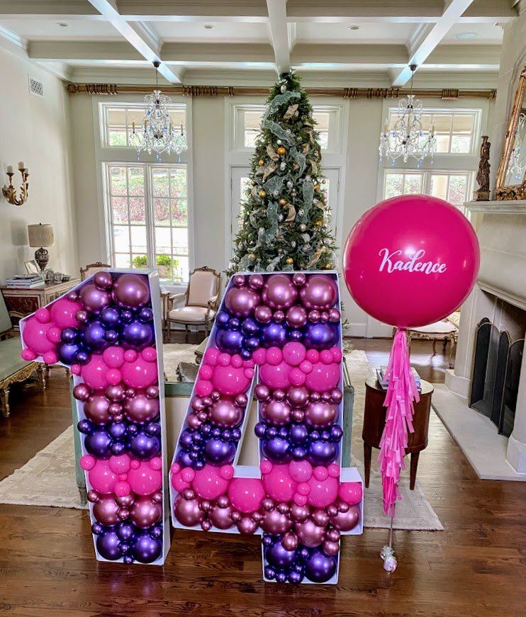 A large number made of balloons in a living room with a christmas tree in the background.