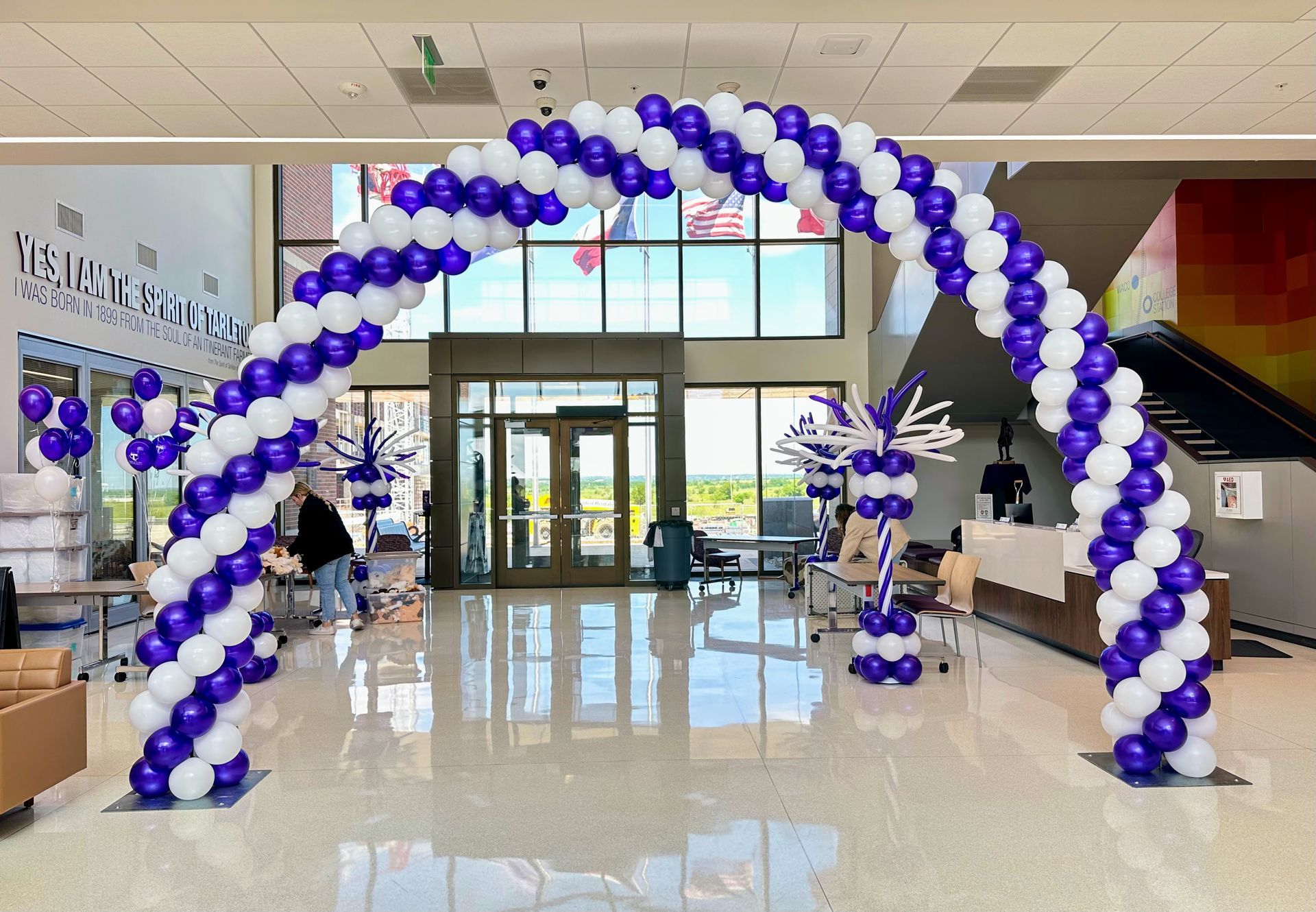 A large arch made of purple and white balloons in a lobby.