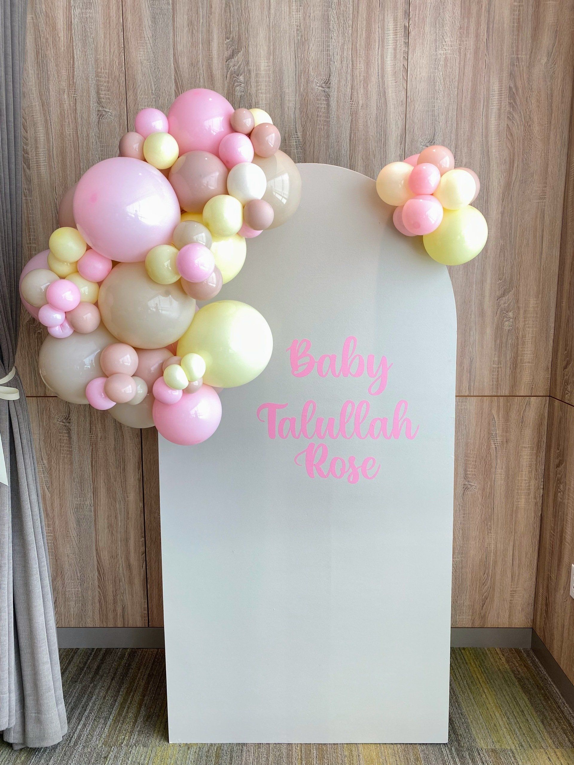 A white sign with pink and yellow balloons on it.