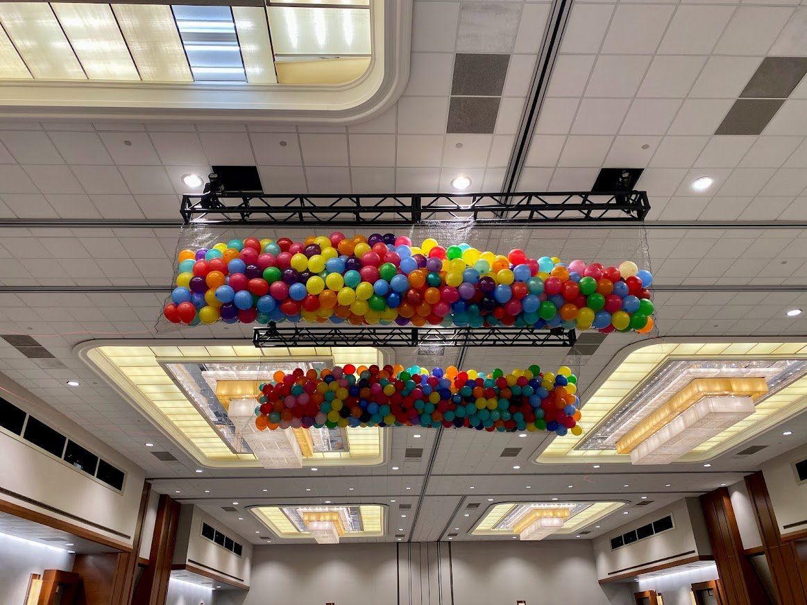 A bunch of balloons are hanging from the ceiling of a large room.