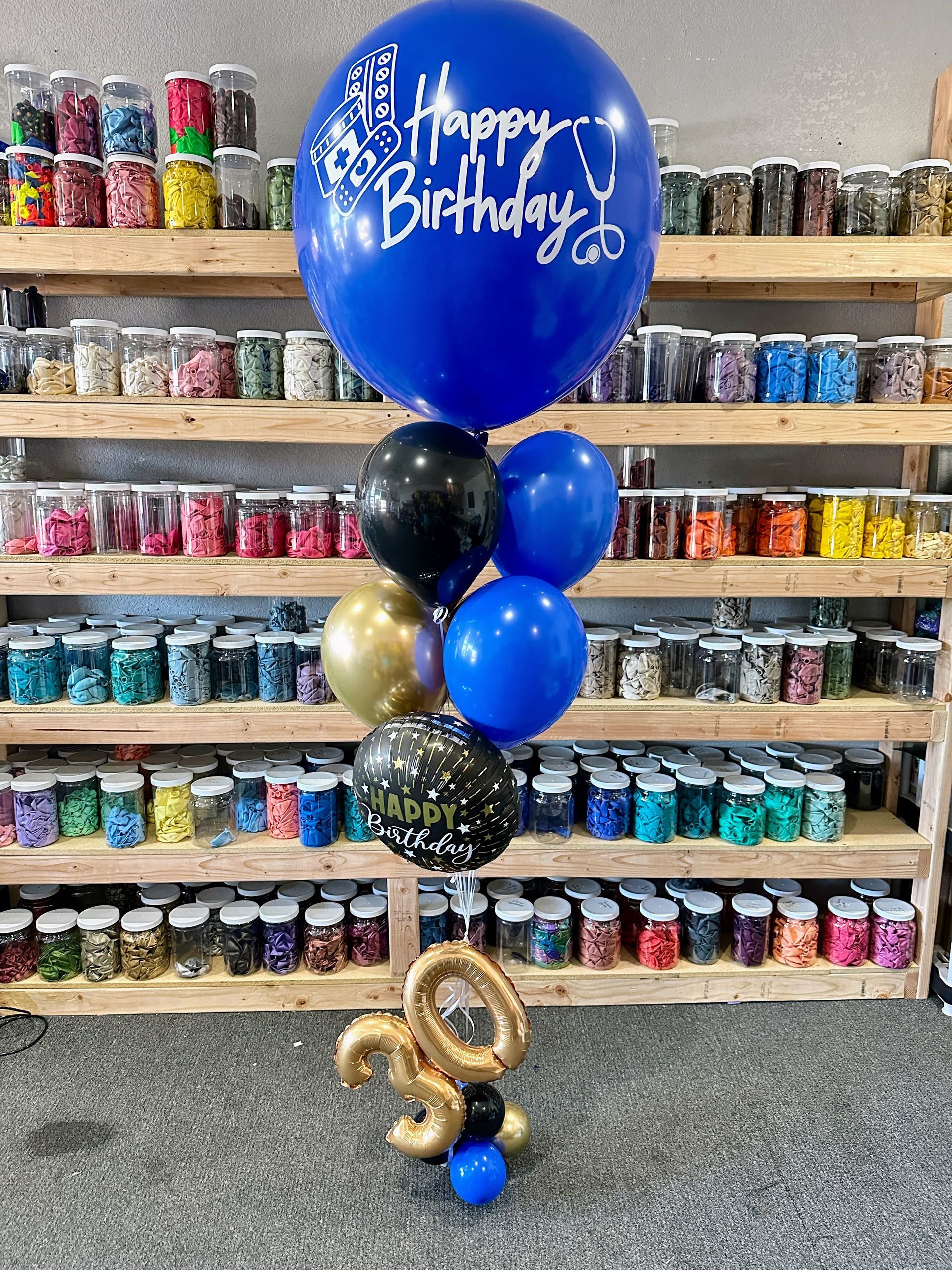 A jumbo helium balloon personalized with Happy birthday for a nurse, with matching blue and black colored tassels.