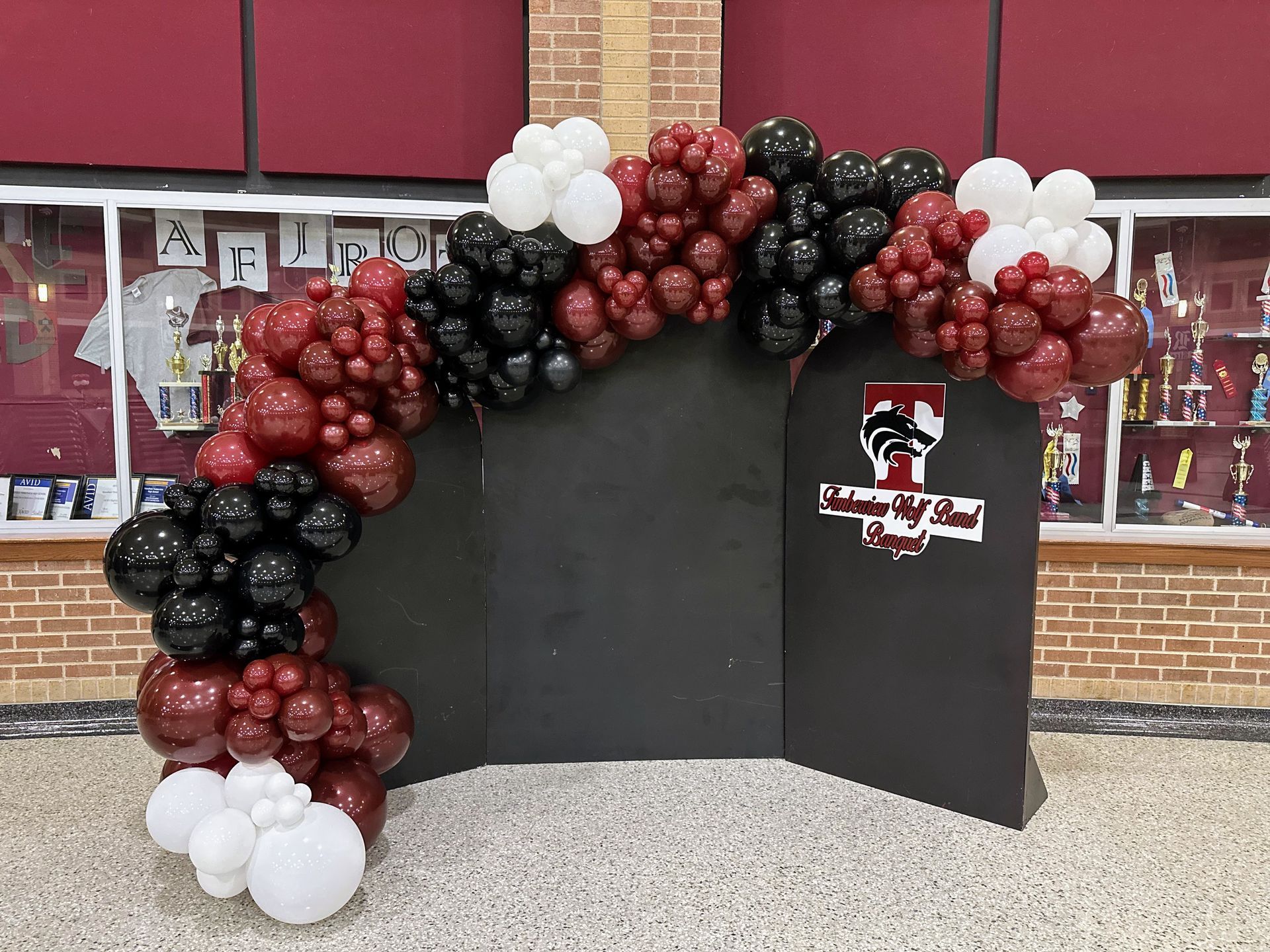 A red , black and white balloon arch is sitting in front of a brick building.