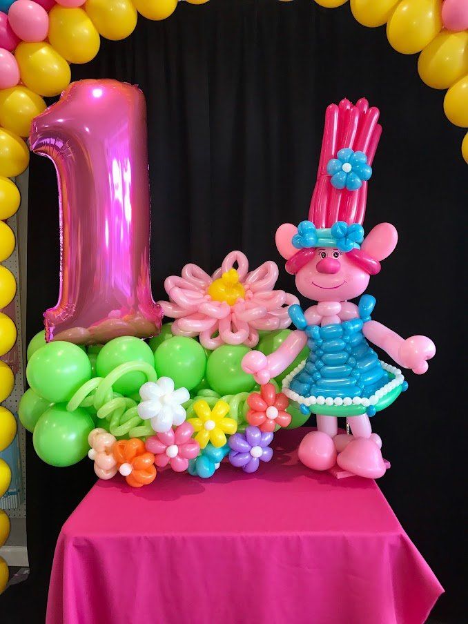 A troll made out of balloons is sitting on a table next to a number one balloon