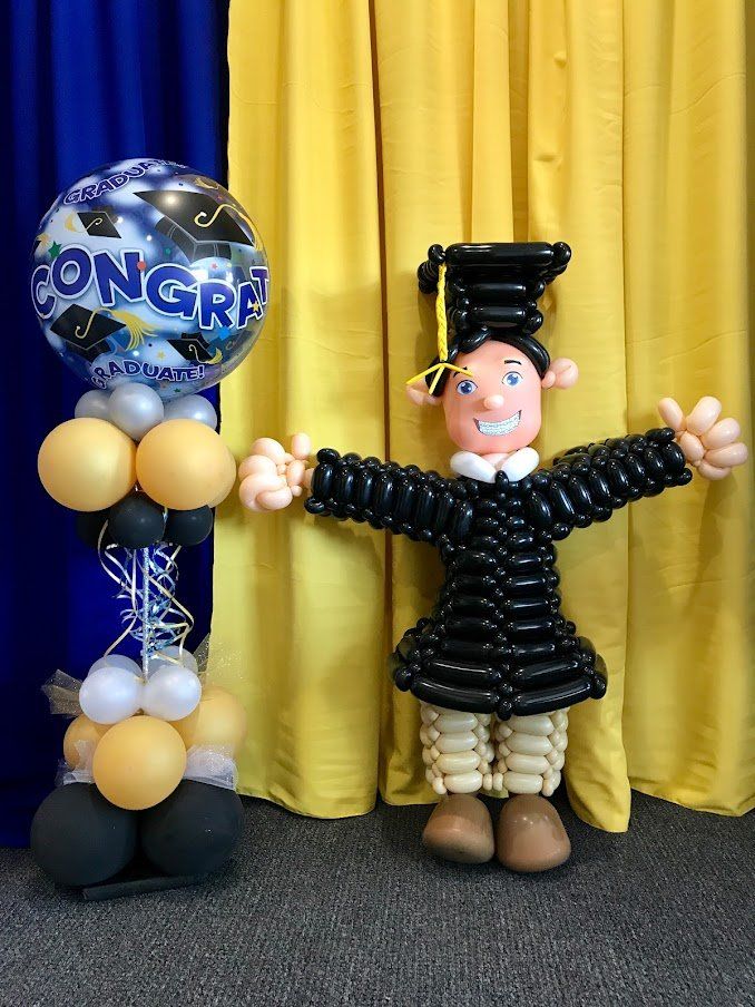 A balloon sculpture of a graduate is standing next to a congratulations balloon.