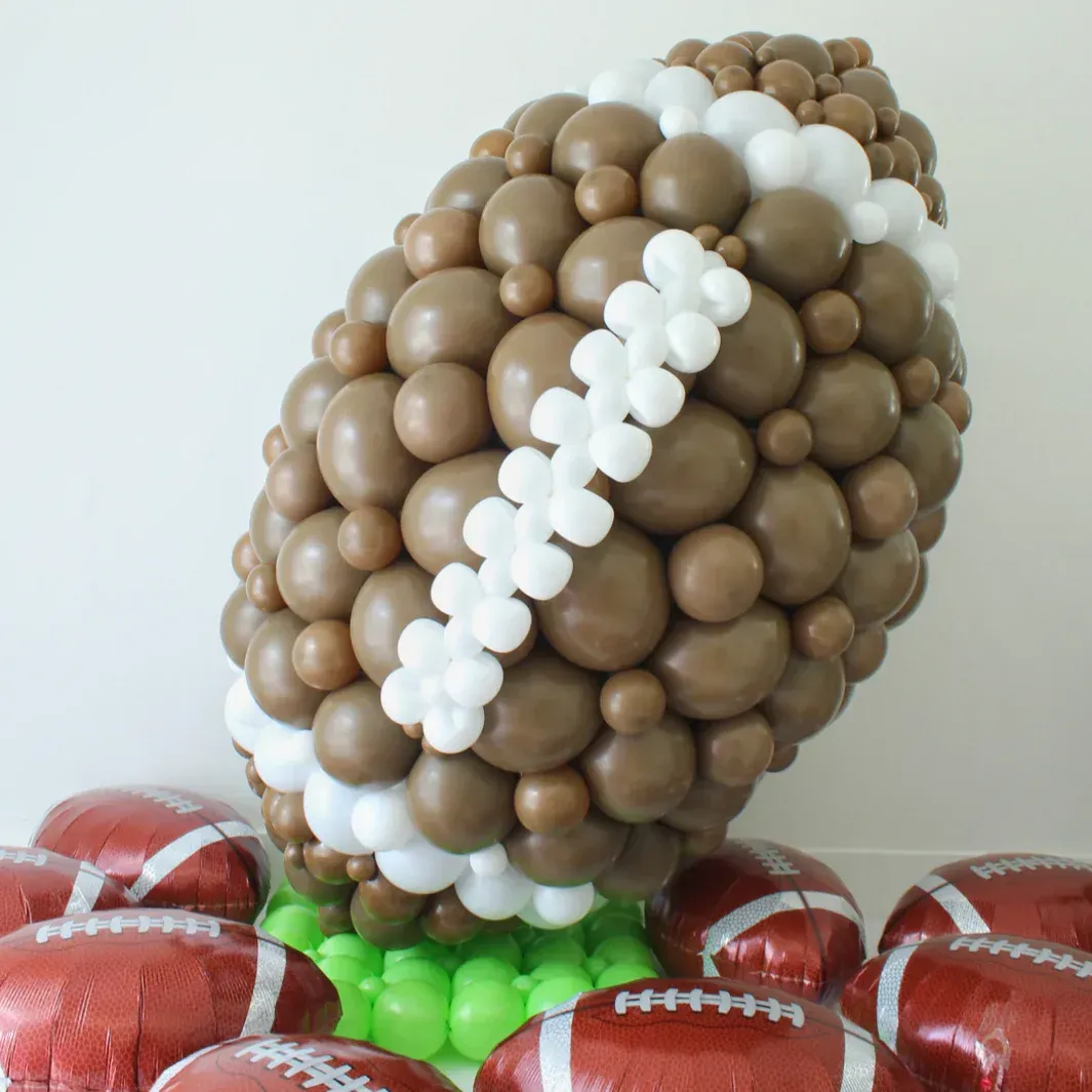 Large Football made out of brown and white balloons on a green balloon base with foil footballs