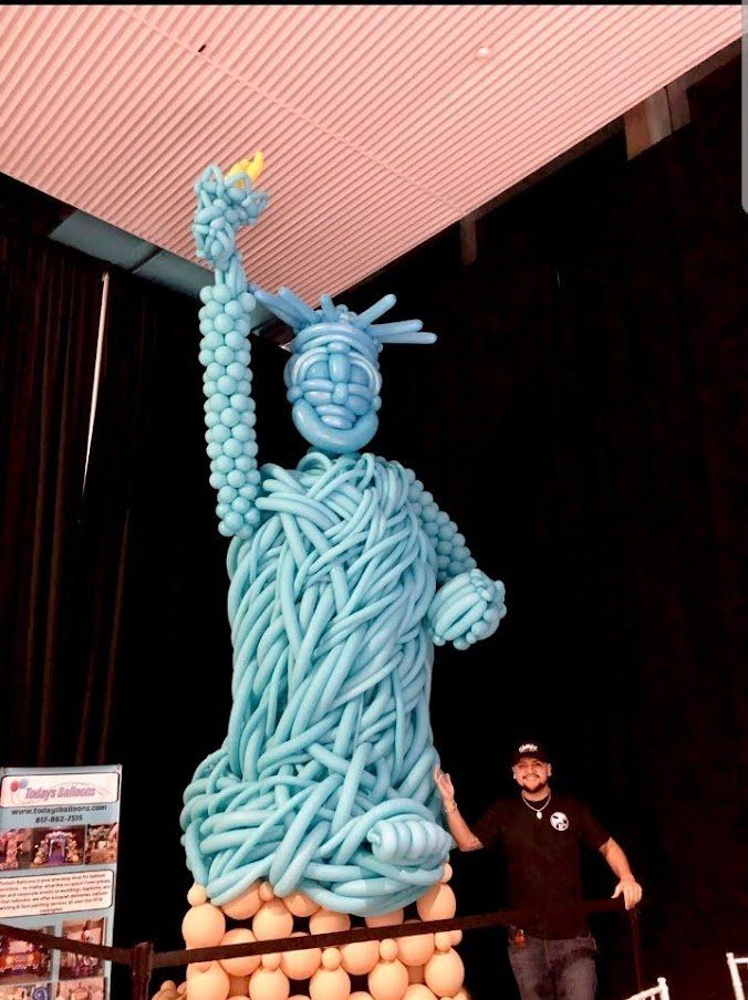 A man standing next to a statue of liberty made of balloons