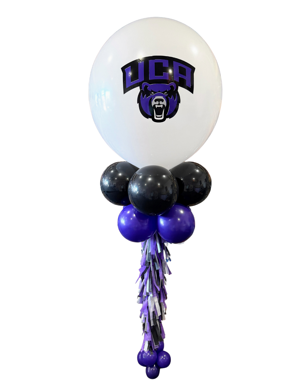 A custom balloon centerpiece featuring a large white latex balloon at the top, prominently displaying the UCA bear mascot logo in purple and black, ideal for school events or college celebrations. Below the main balloon, clusters of shiny black and vibrant purple balloons form the base, complementing the institution's colors. A decorative tassel garland in shades of purple, grey, and black drapes elegantly from the mid-section, leading to a cluster of small purple balloons at the bottom. This impressive balloon column is perfect for university graduation parties, sports events, alumni gatherings, or any occasion requiring branded event decor and school spirit decorations