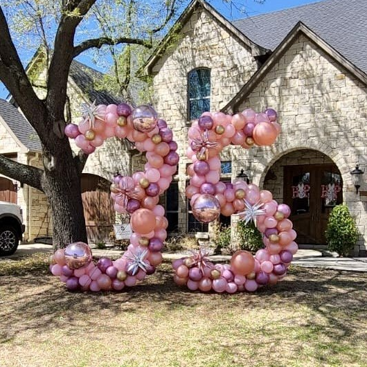 A large number 35 made of pink and purple balloons in front of a house.