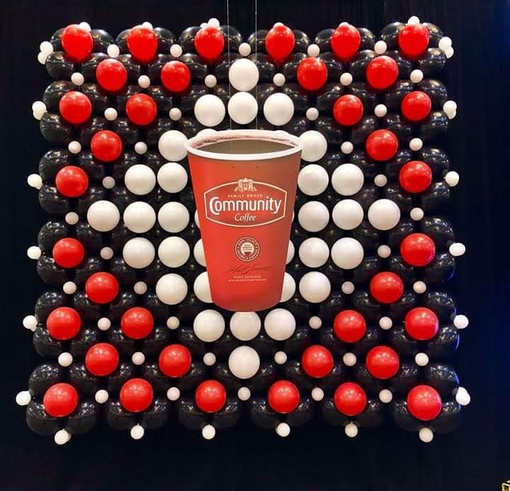 A cup of community coffee is surrounded by red and white balloons