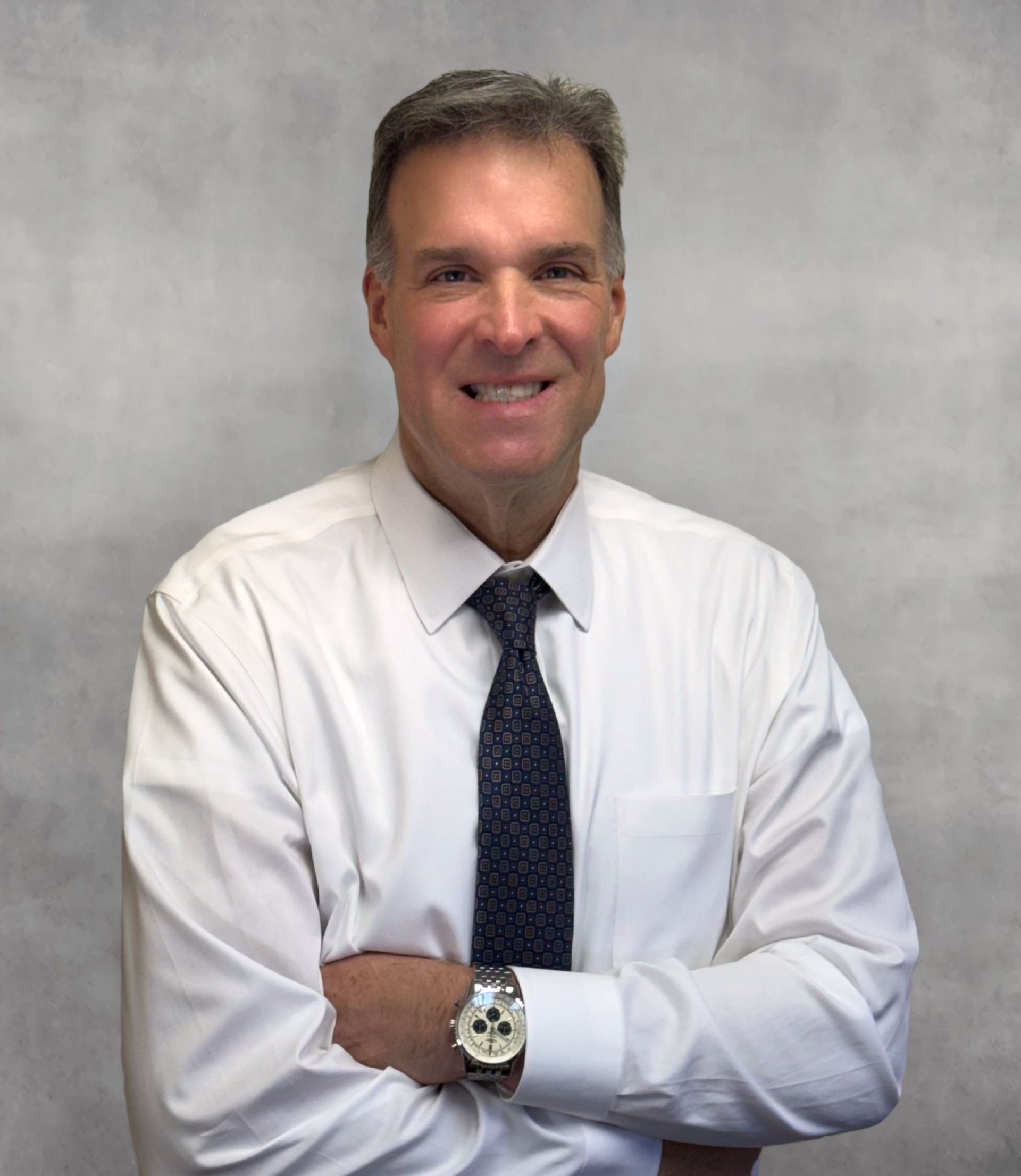Man in white shirt and tie smiling with arms crossed, watch visible.