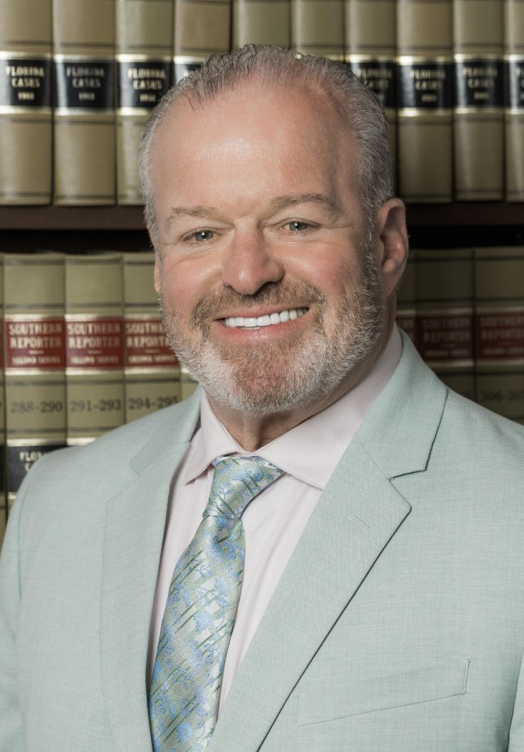 Smiling man in light gray suit and tie standing before a bookshelf of law books