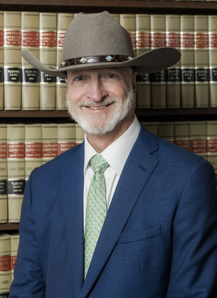 Man in blue suit and cowboy hat standing before shelves of law books, smiling