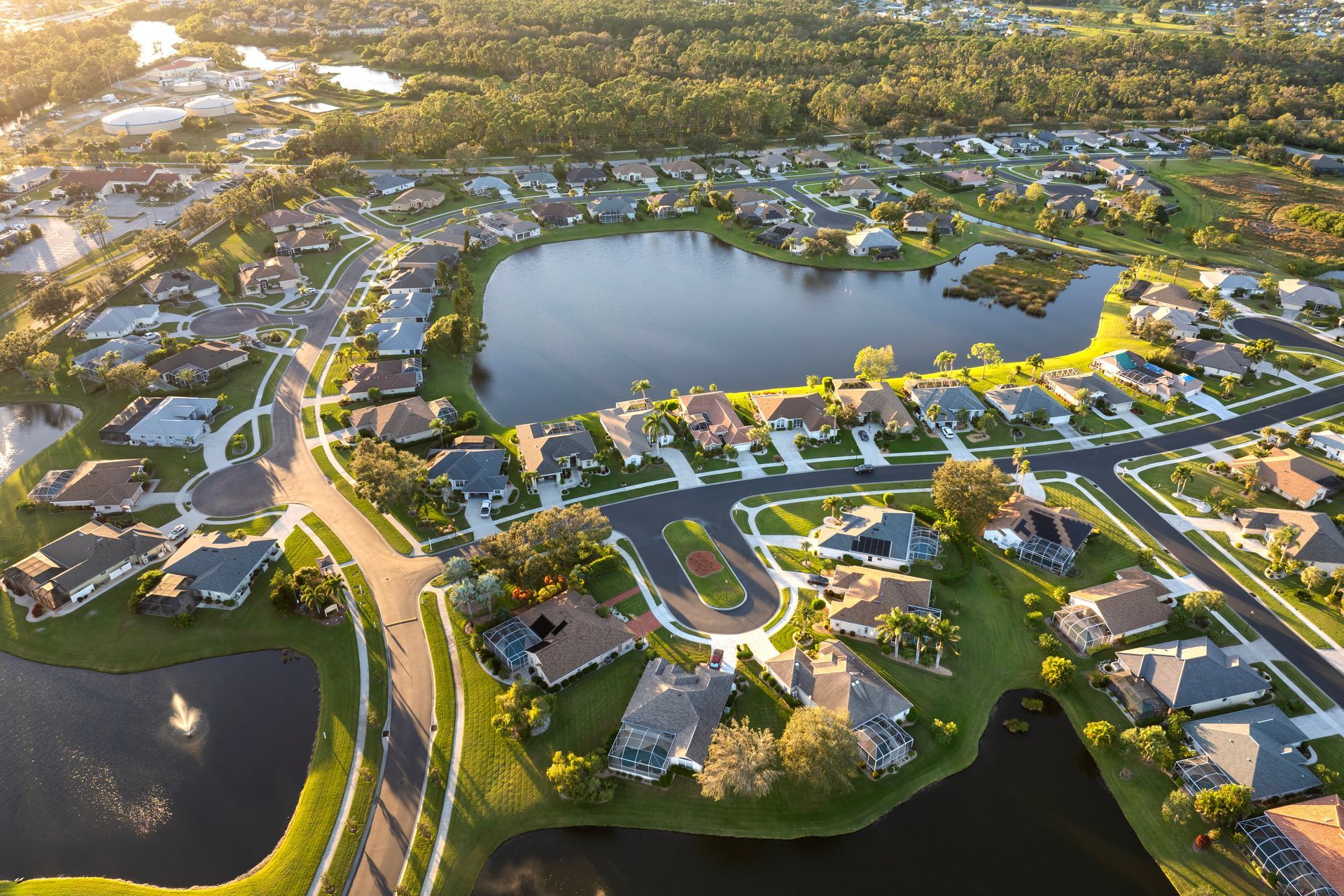Aerial view of a residential neighborhood with houses clustered around several ponds under golden sunlight.