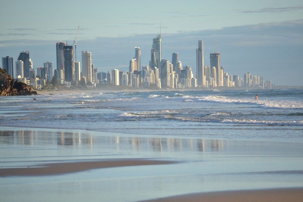 A City Skyline Is Reflected In The Water Of A Beach — Salt Building & Pest Inspections in Burleigh Heads, QLD