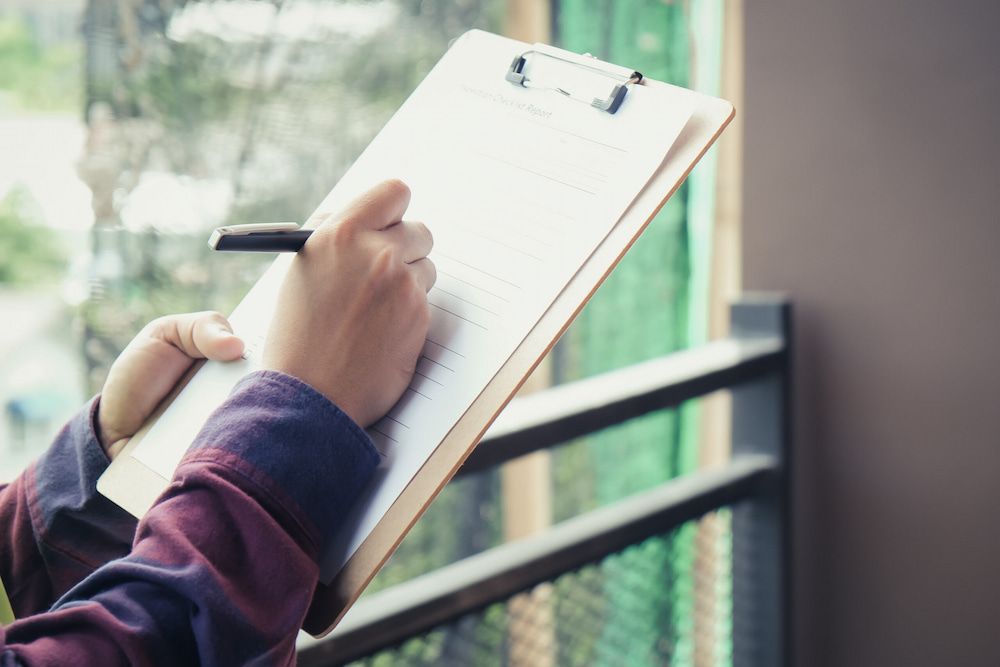 A Person Is Writing On A Clipboard With A Pen — Salt Building & Pest Inspections in Clear Island Waters, QLD