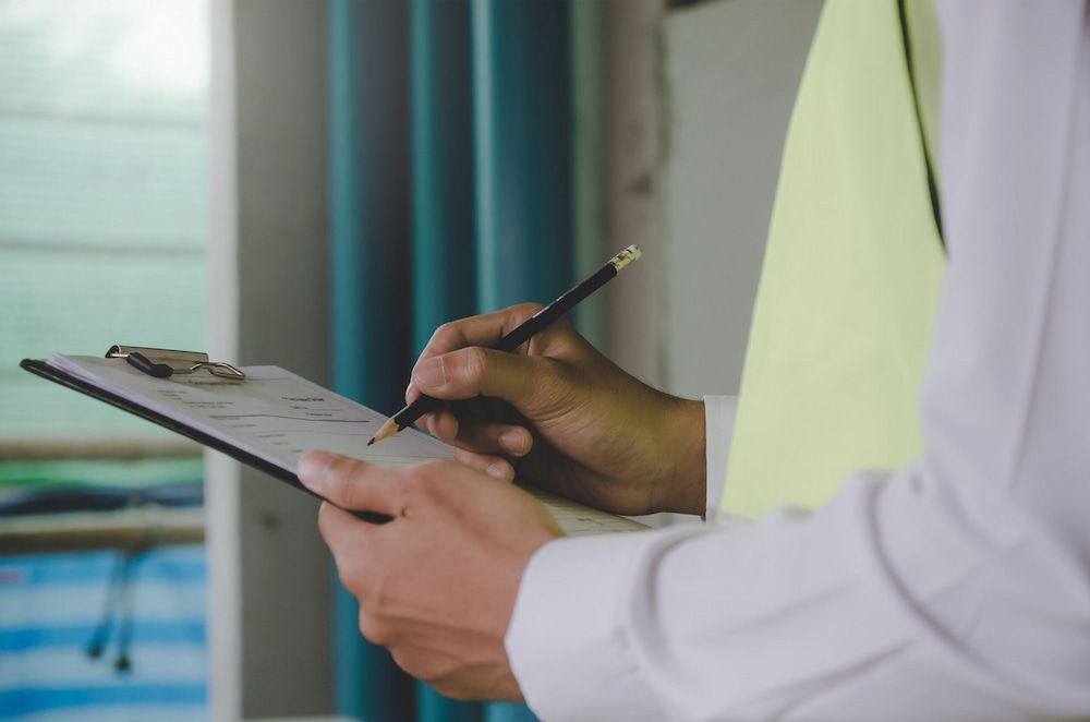 A Man Is Writing On A Clipboard With A Pencil — Salt Building & Pest Inspections in Carrara, QLD