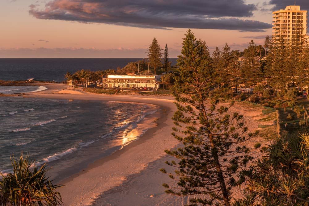 A View Of A Beach At Sunset With A Building In The Background — Salt Building & Pest Inspections in Coolangatta, QLD