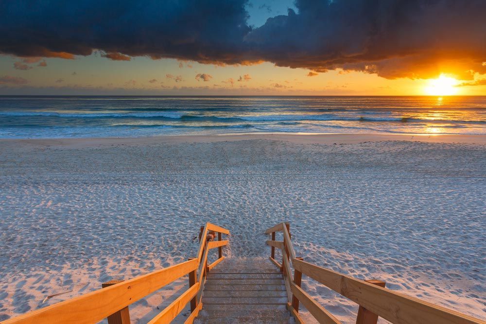 A Wooden Walkway Leading To The Beach At Sunset — Salt Building & Pest Inspections in Mermaid Beach, QLD
