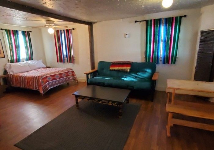 A motel room with a bed, dresser, and a small table. The room has a neutral color palette with green accents.