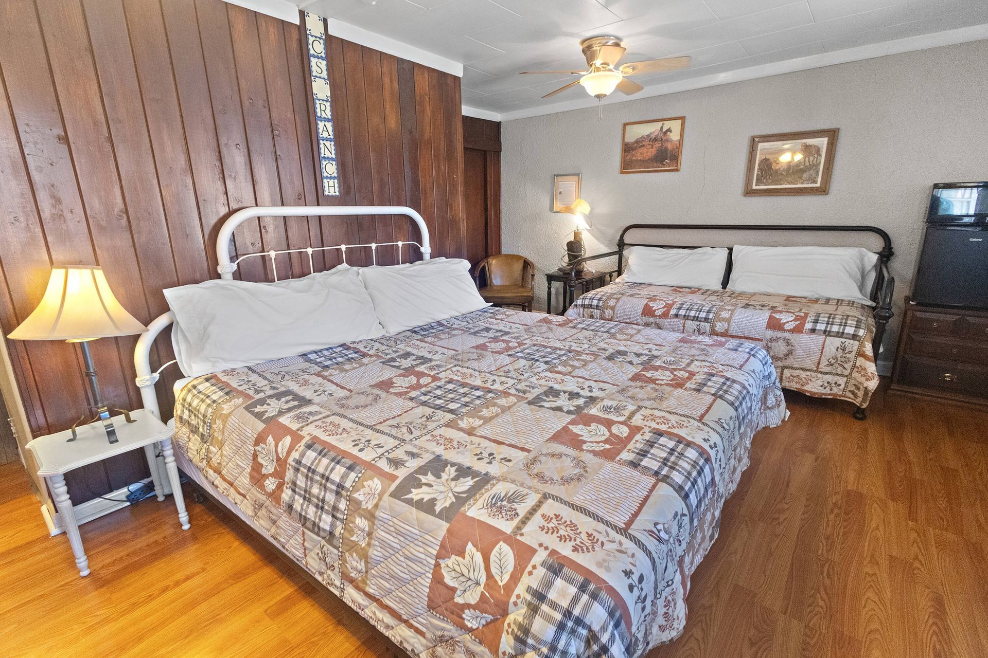 Hotel room with a bed, TV, dresser, microwave, and view of the bathroom. Green and brown bedspread, tan walls.