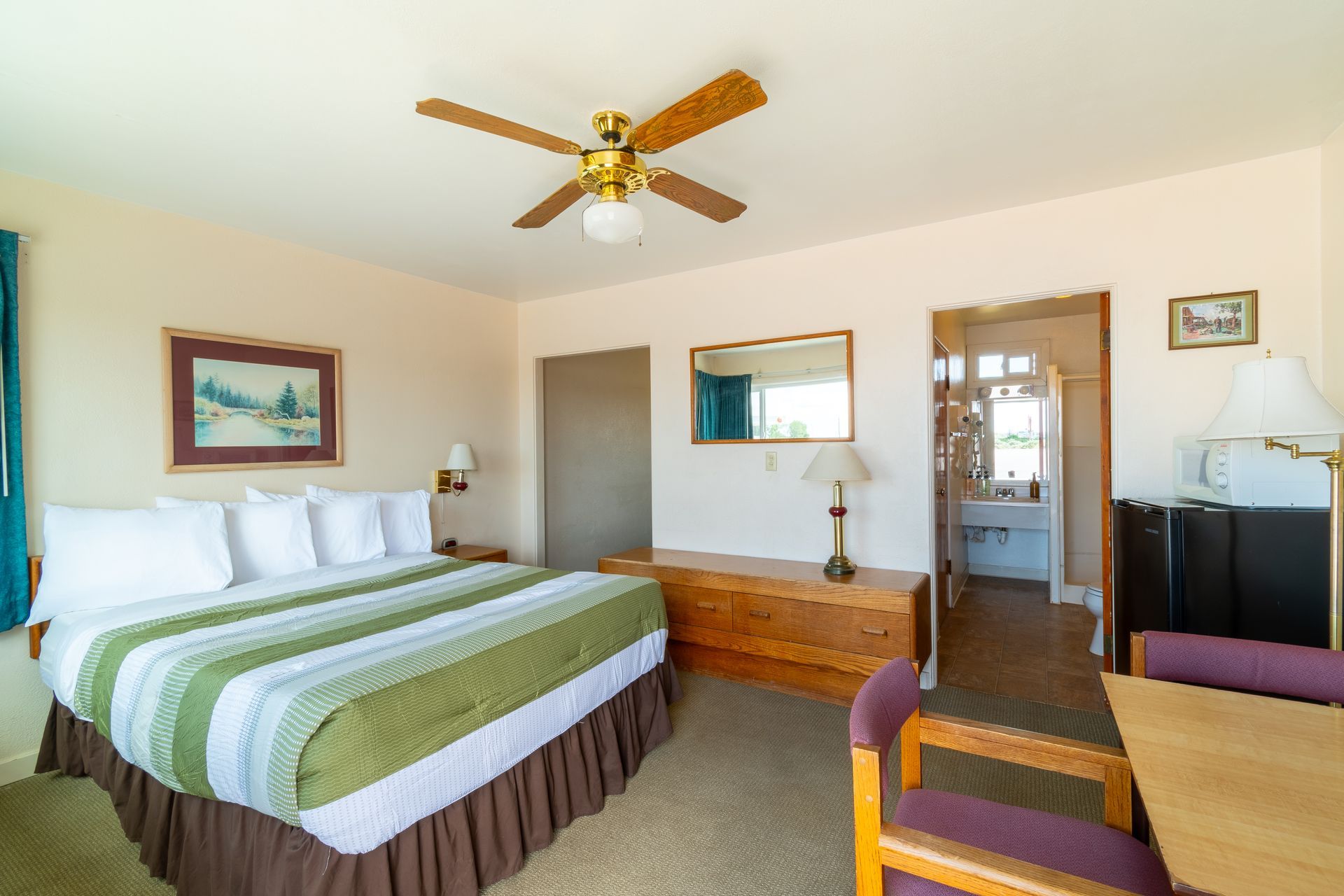 A motel room featuring a bed, dresser, table, and an open doorway to the bathroom.