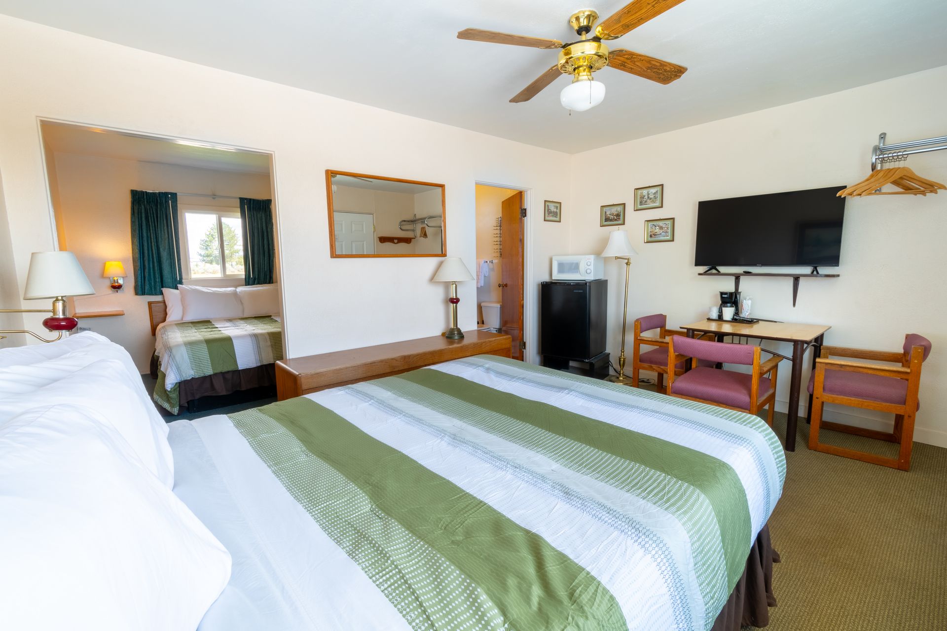 A motel room with two beds, a TV, a microwave, and a small table and chairs. One bed has green and white striped bedding.