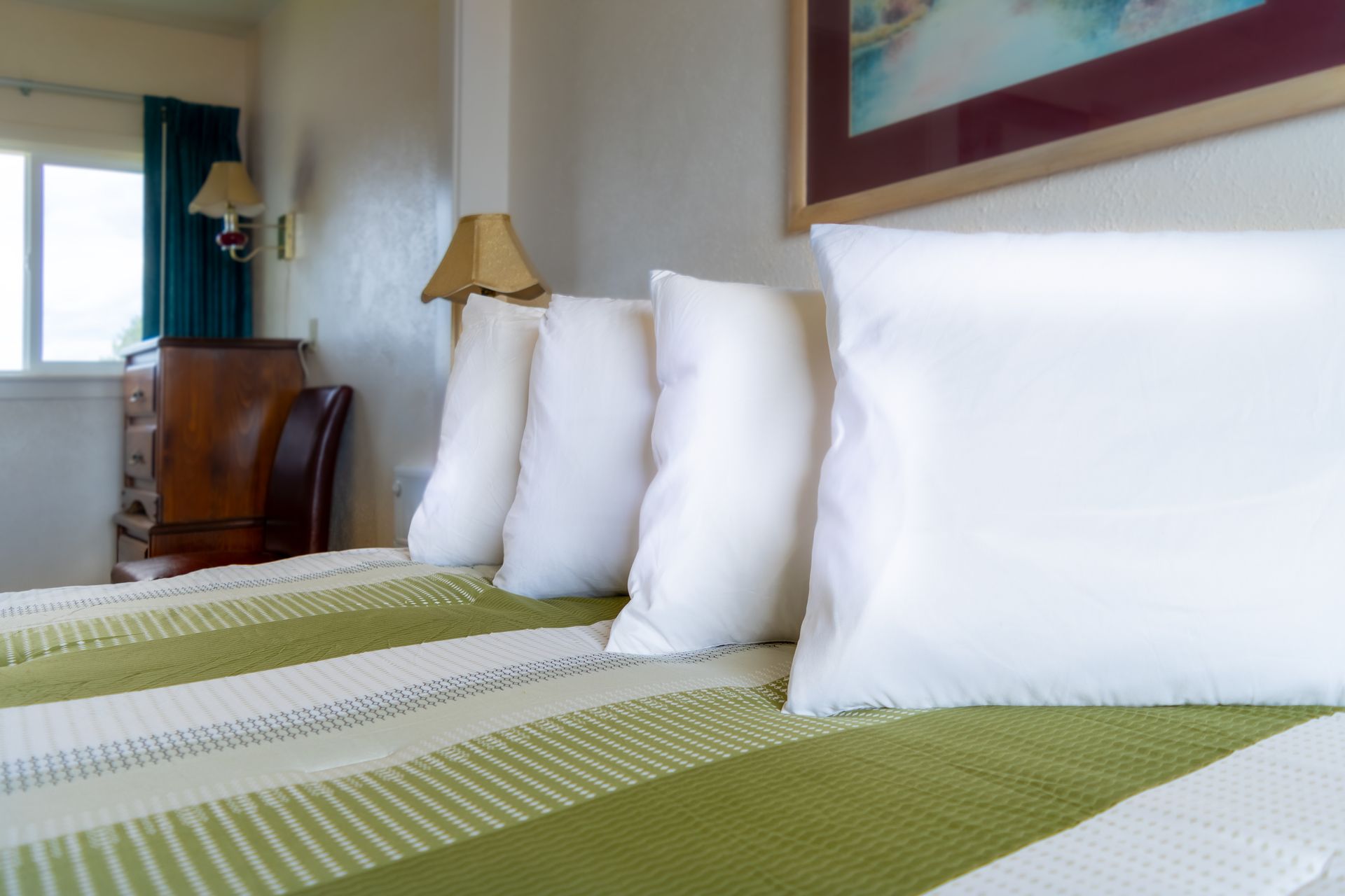 A bed with white pillows, a green and white striped blanket, and a chest of drawers in a room with a window.