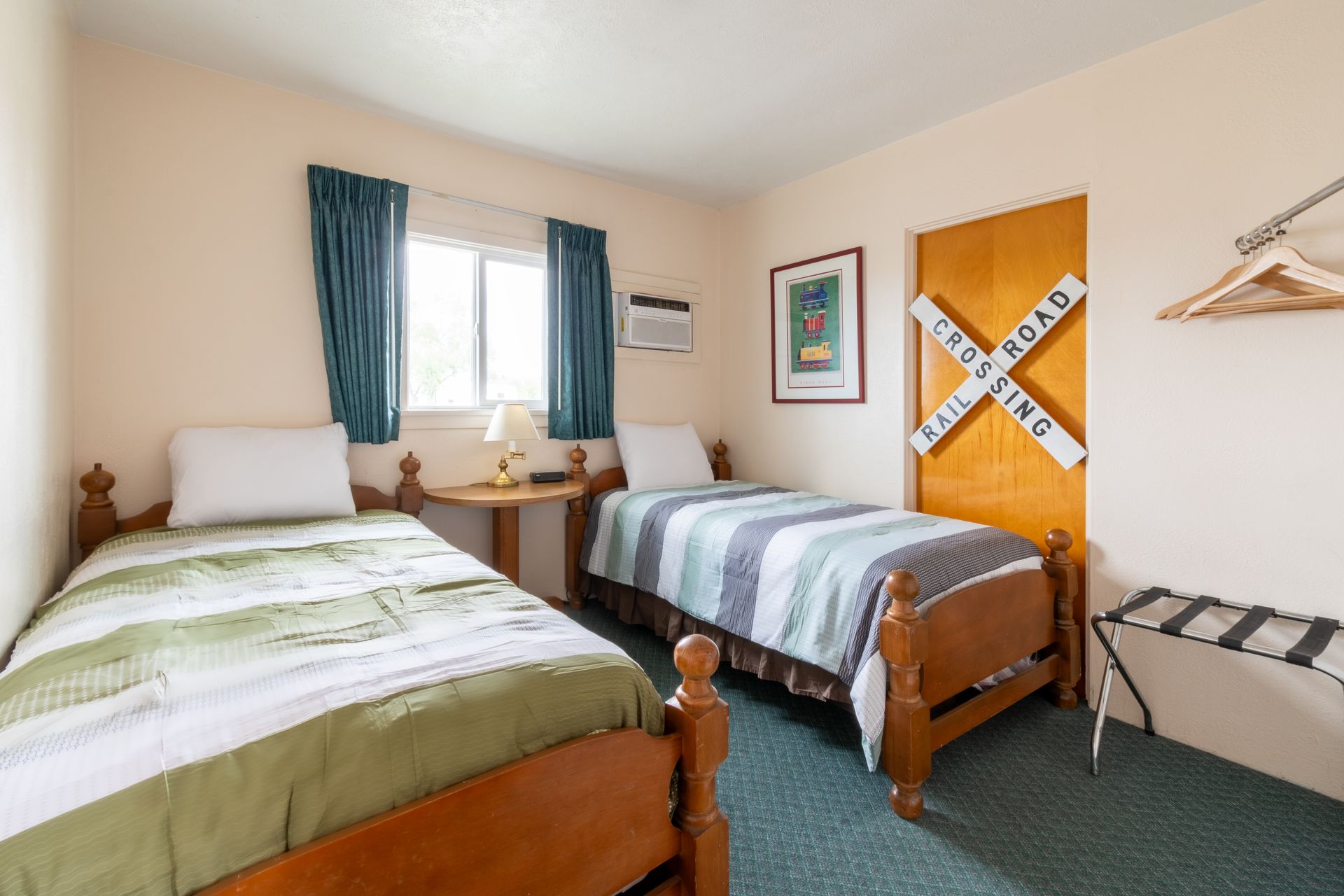 Two twin beds in a motel room with a railroad crossing sign on the door. Beds have green and blue patterned bedding.