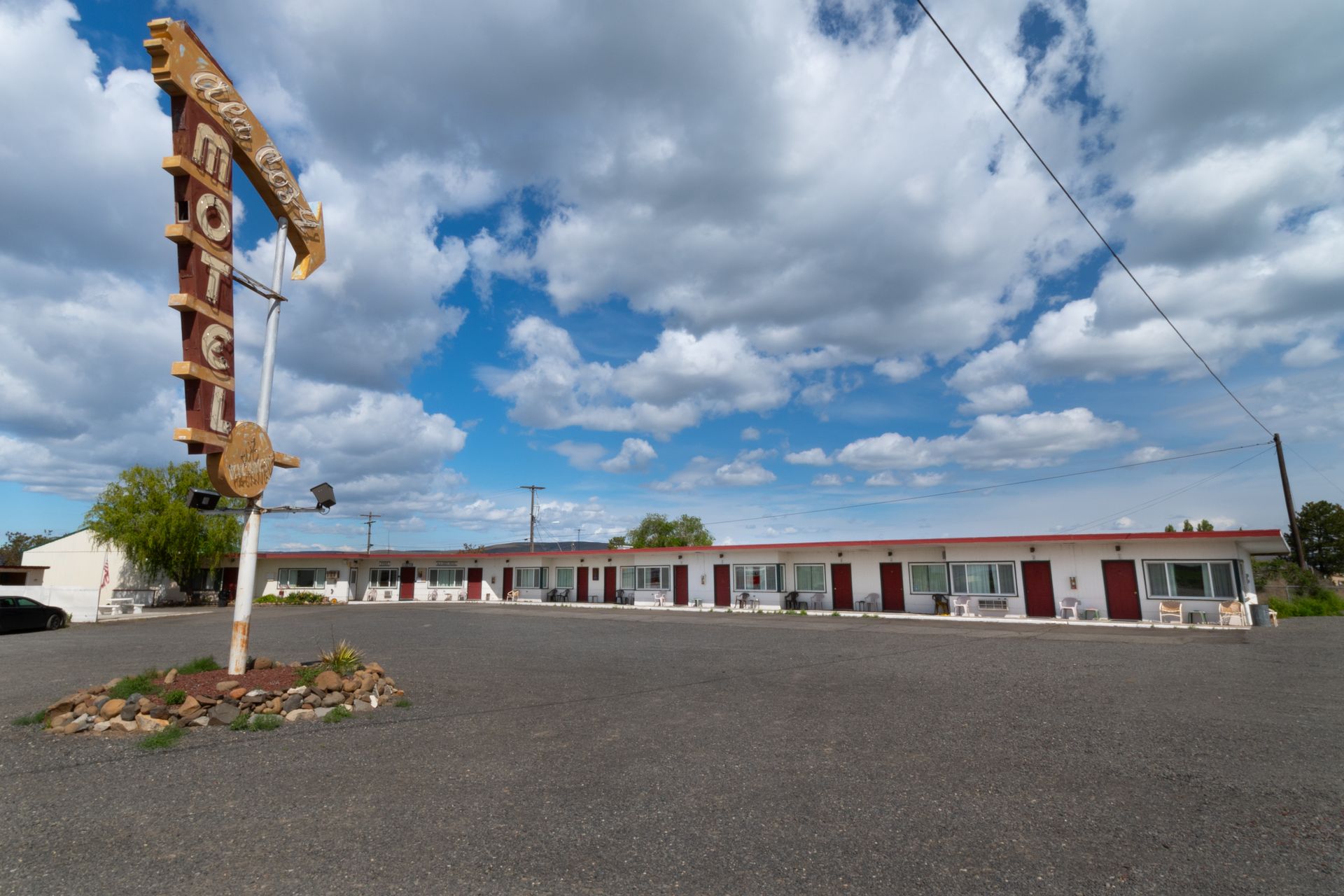 A vintage motel with a tall sign under a partly cloudy sky. Motel rooms are one-story with red doors.
