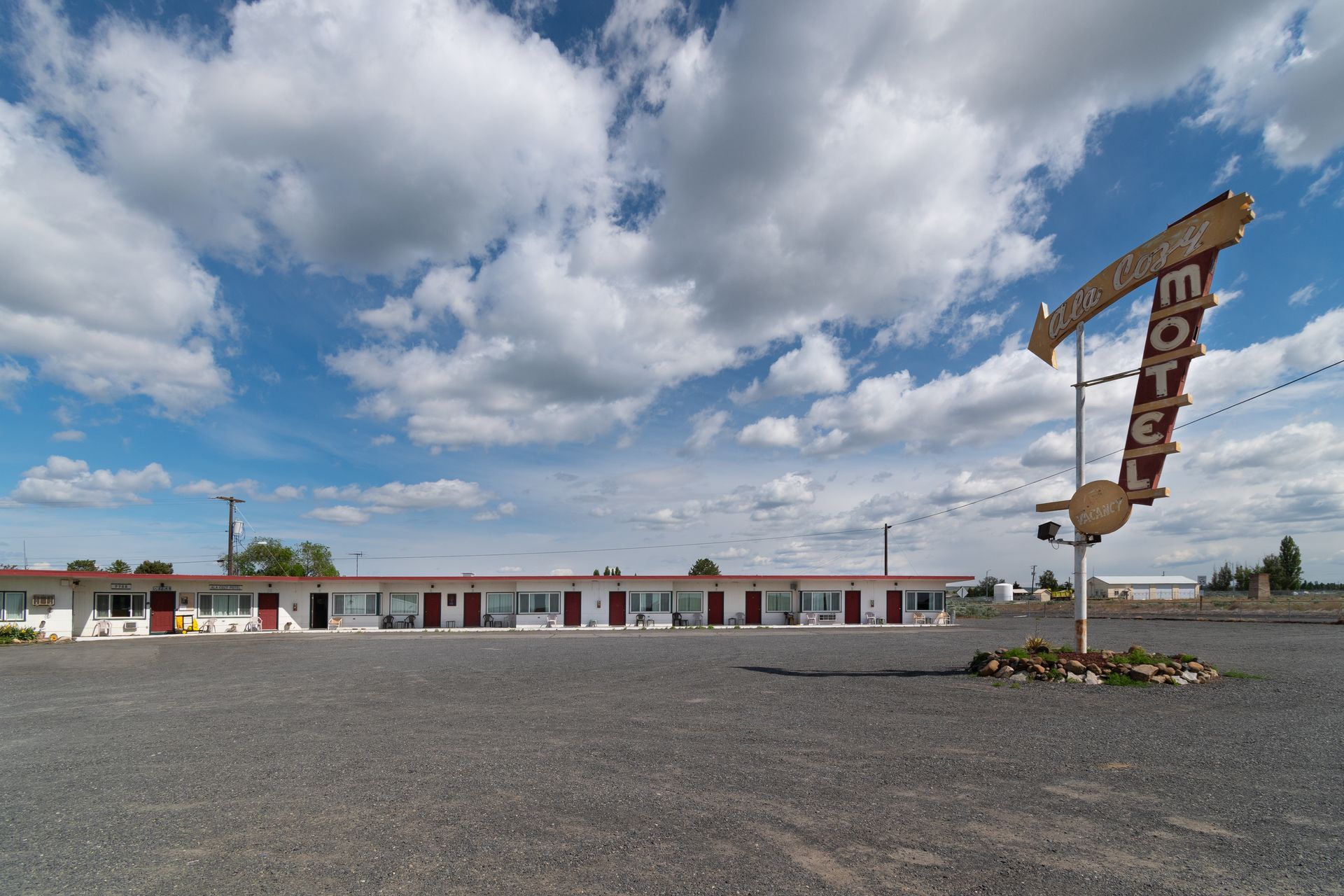 A rundown motel with a tall, faded sign against a blue sky dotted with fluffy white clouds.