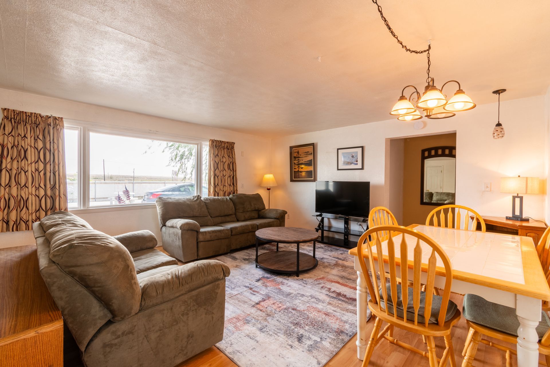 Living room with a sofa, armchair, dining table, and television. The room has a neutral color palette with wood accents.