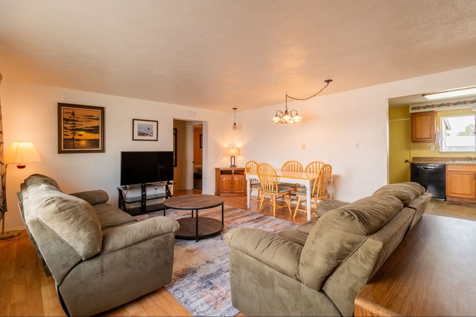 Living room with green sofas, a round coffee table, a dining table, and a kitchen visible.