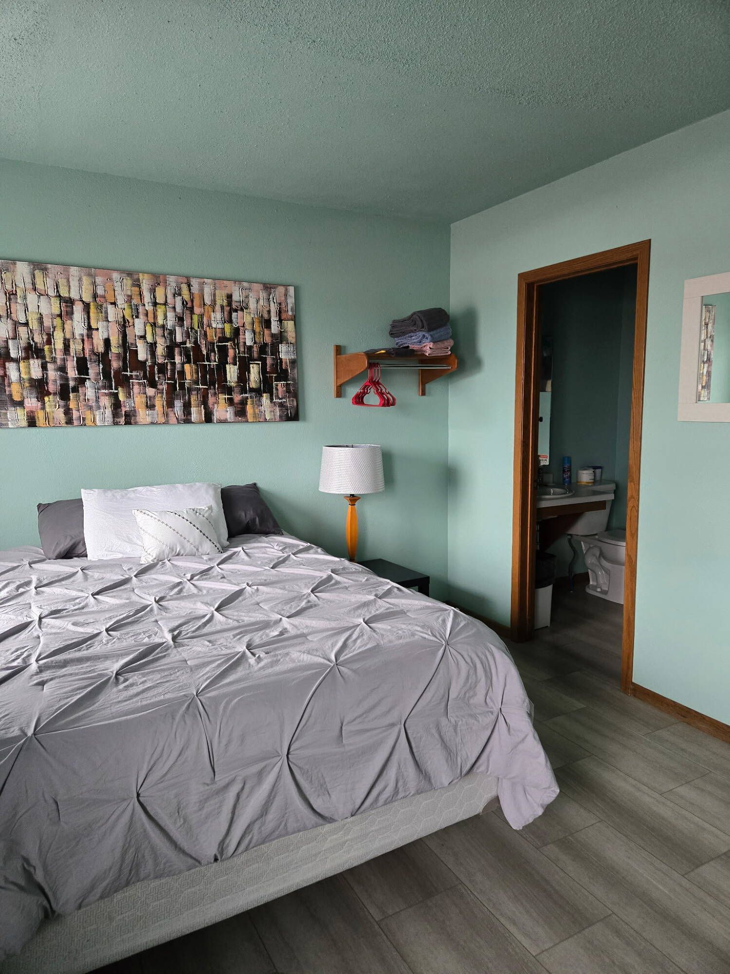 A wooden bed with a white comforter and yellow pillow in a bedroom with a nightstand and shelf.