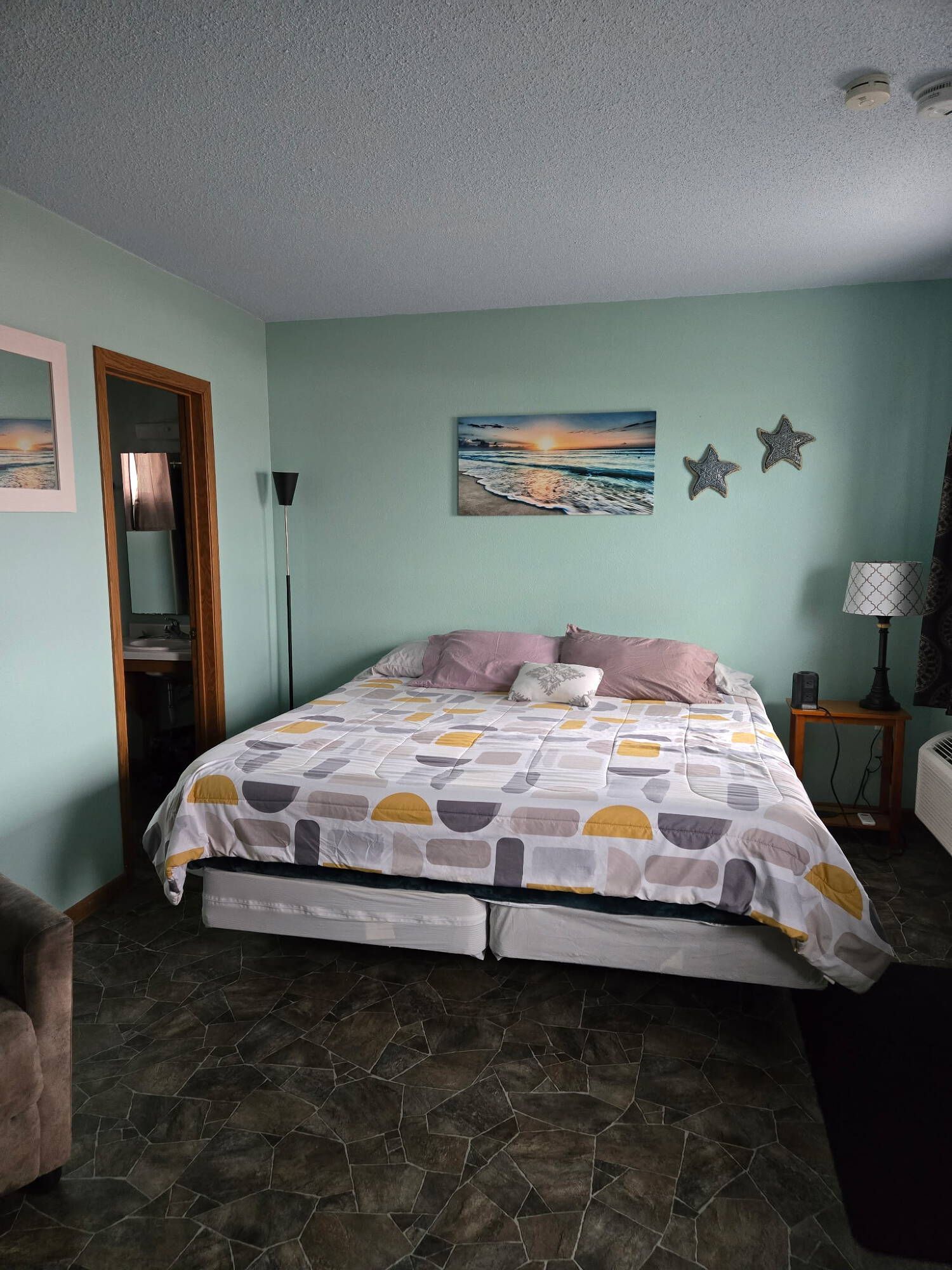 A bedroom with a wooden rocking chair, lamp on a nightstand, and a bed with white linens.