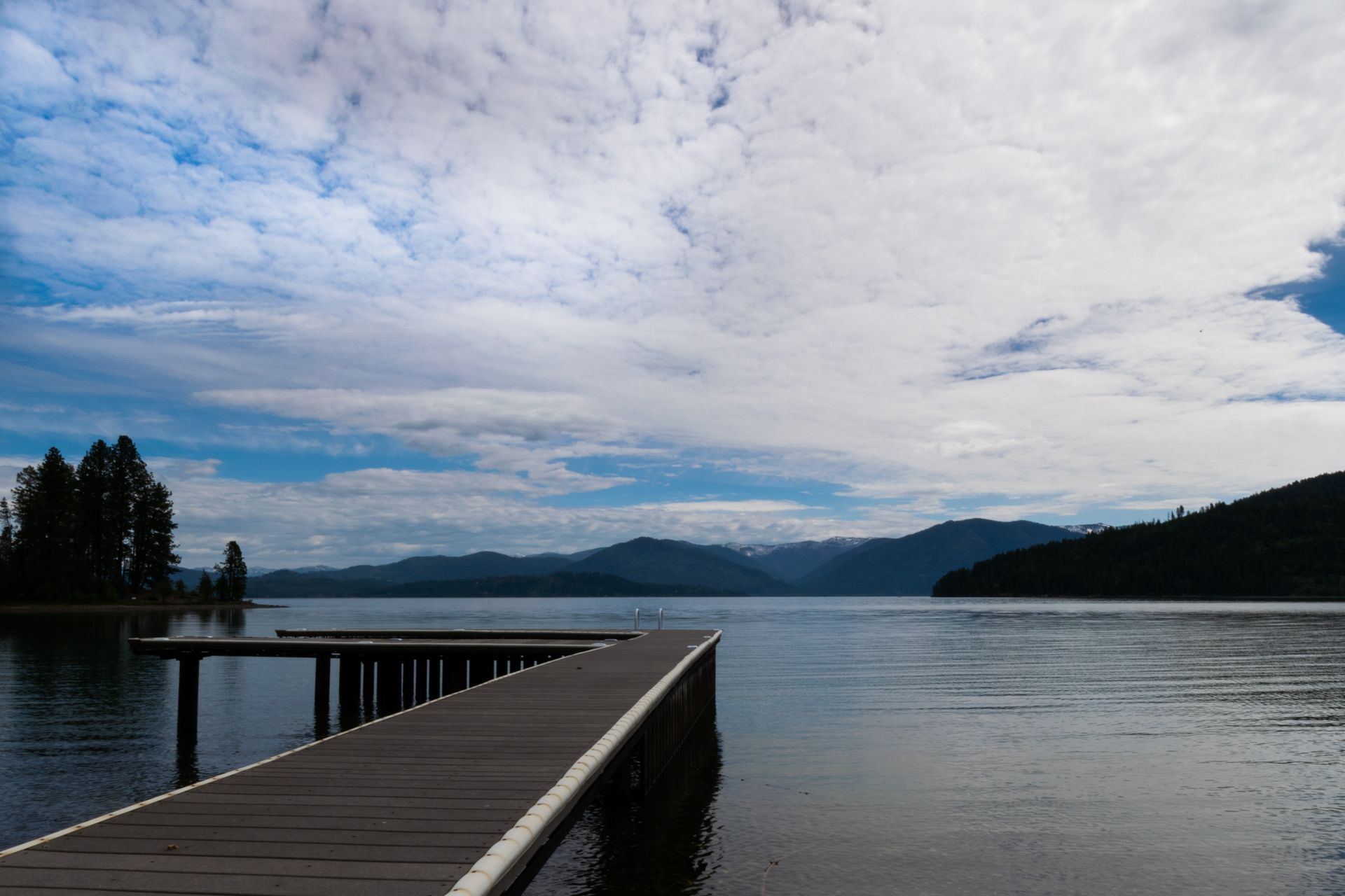 Wooden pier extending into a calm lake, mountains in the distance under a cloudy sky.