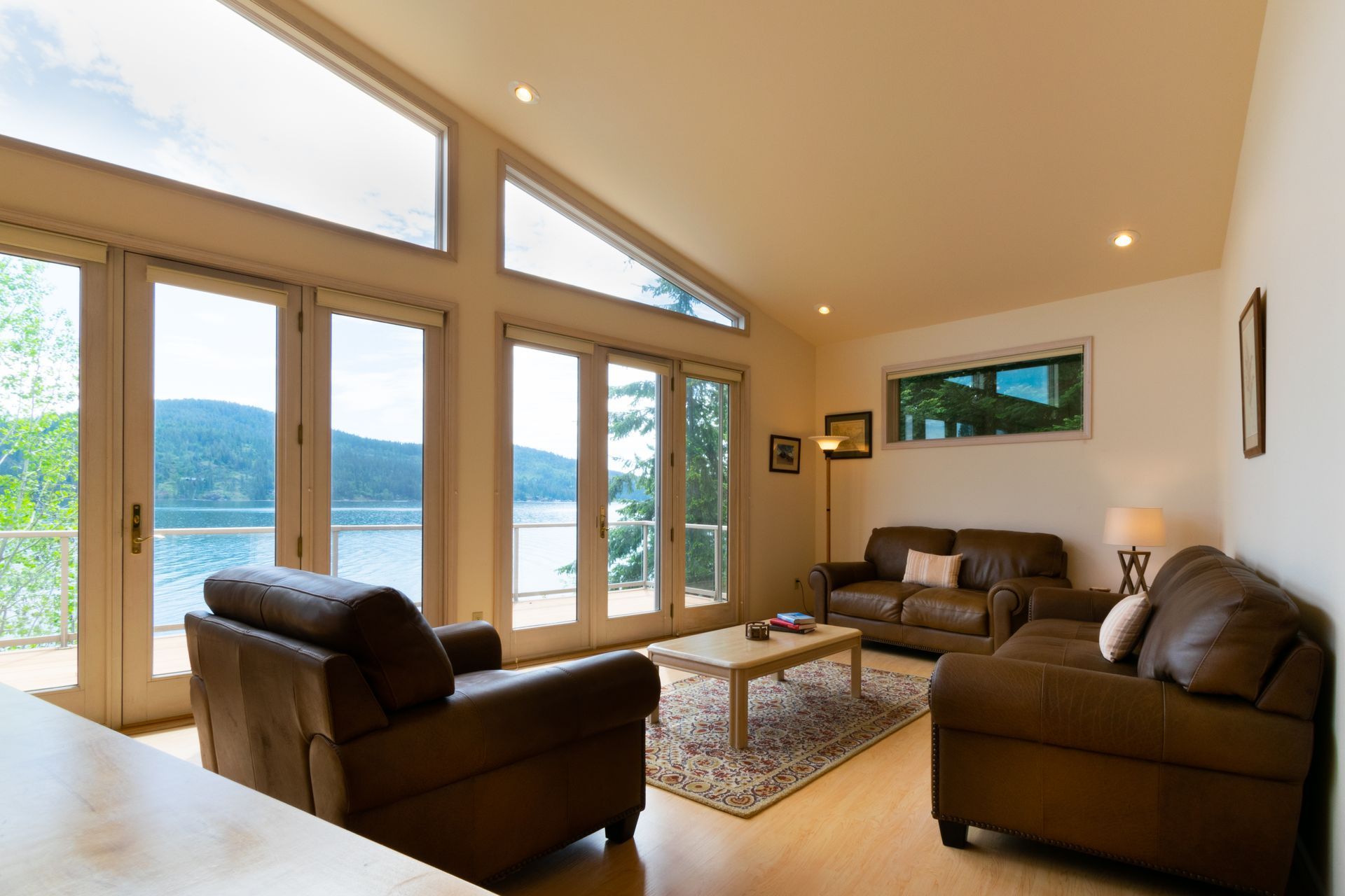 Living room with lake view, featuring brown leather sofas, large windows, and natural light.